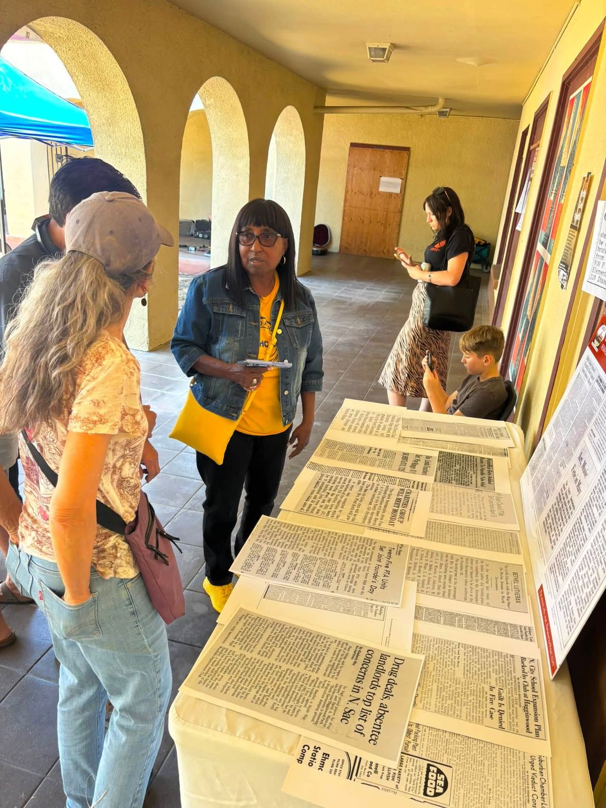Visitors reading newspaper clippings about the school laid out on a long table under the arcade
