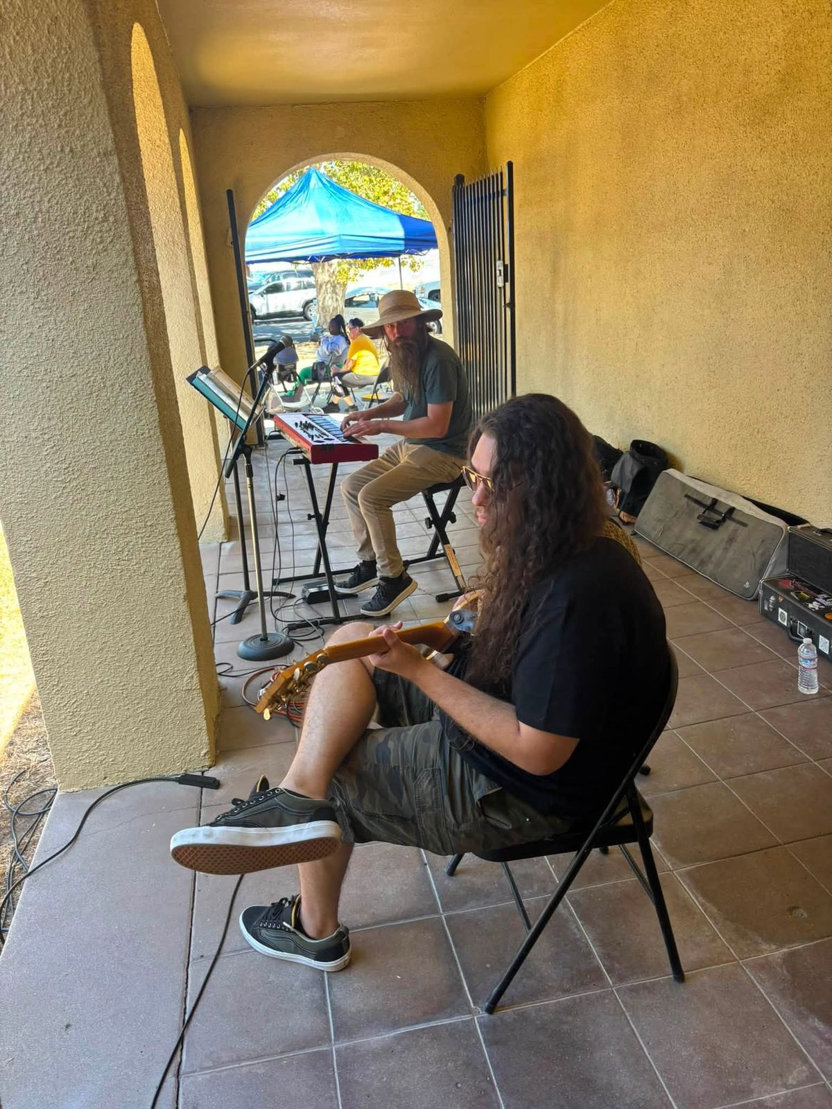 A keyboard player and a guitarist performing under the arched arcade